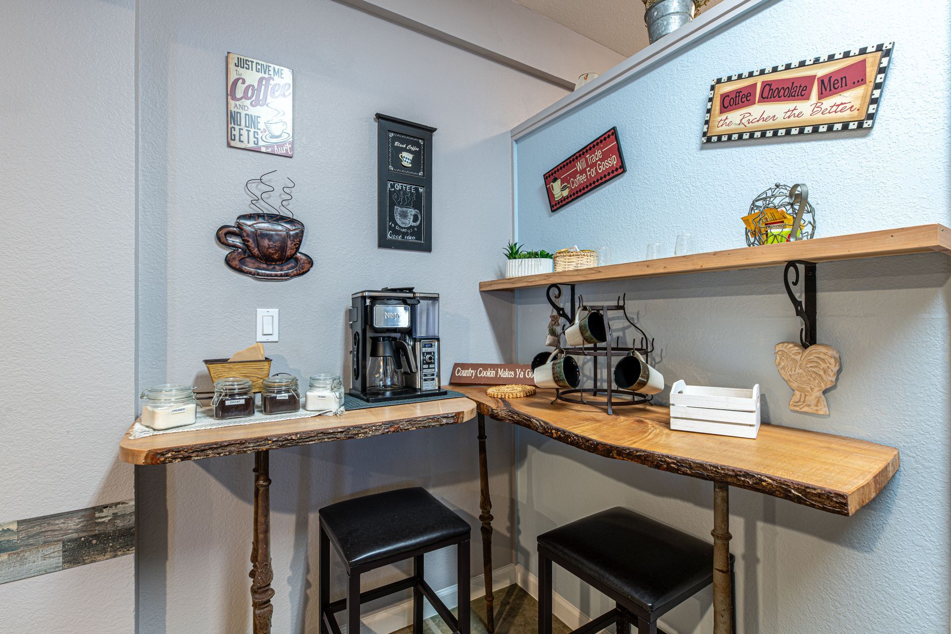 Coffee bar with wooden countertops, black stools, and decorative signs on a gray wall.