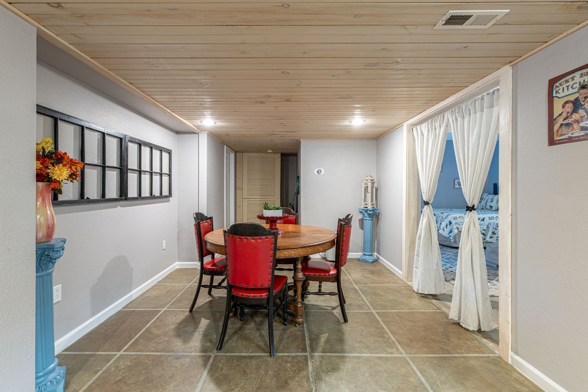 Dining room with a wooden table, red chairs, and a window with white curtains.