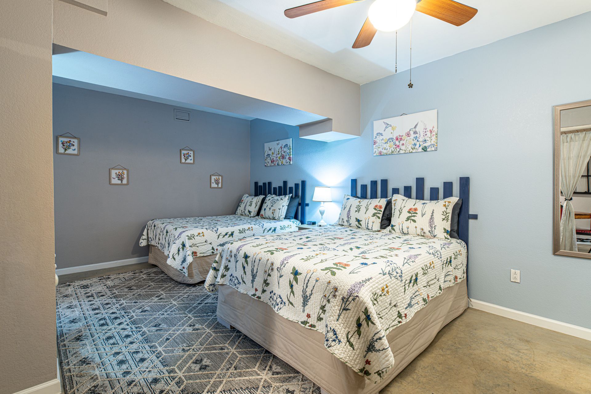 Two beds in a room with blue walls, a rug, and a ceiling fan.
