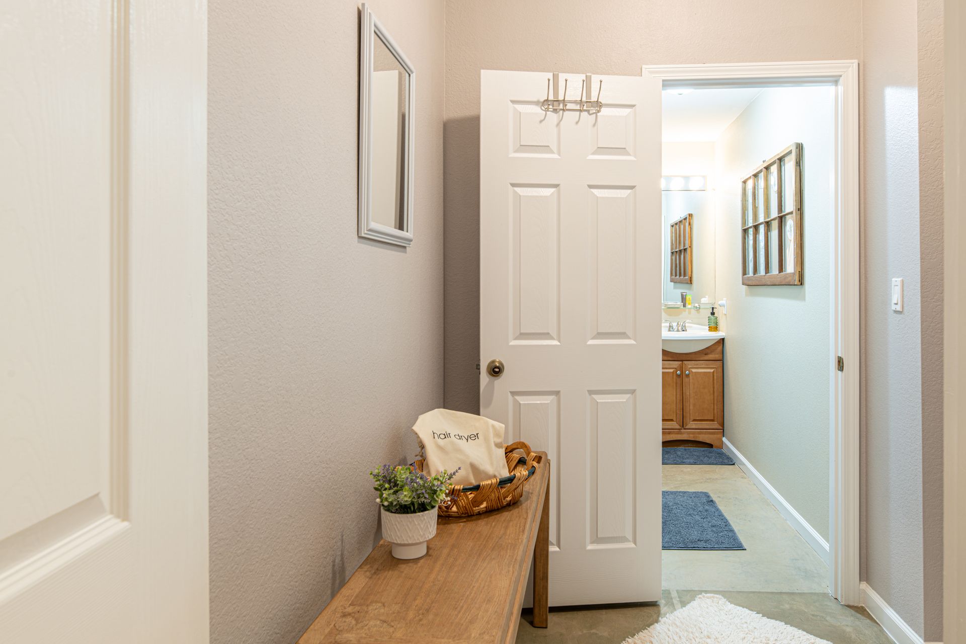 Hallway with wooden bench, open door to bathroom, mirror, and decor.