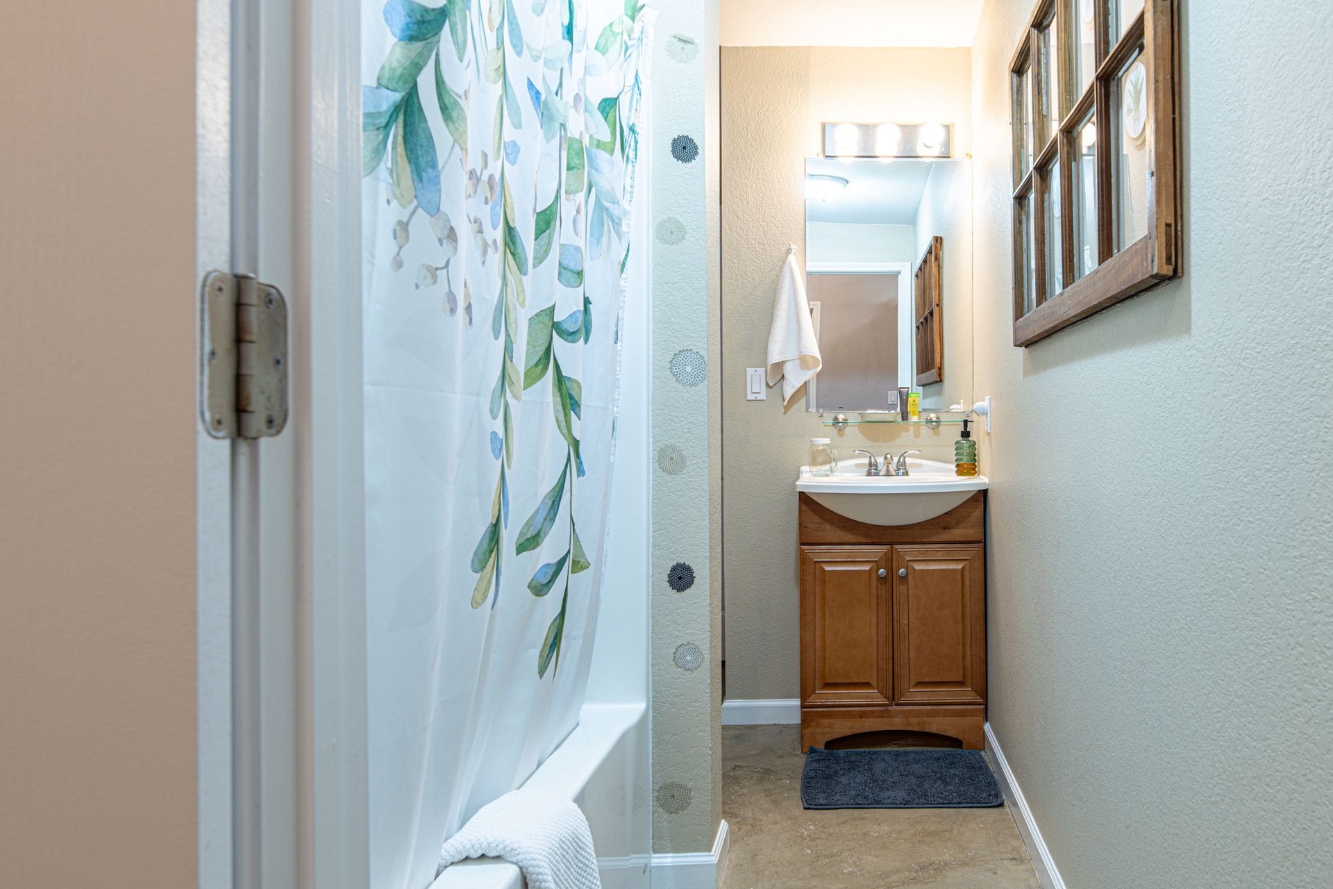 Bathroom with a shower, vanity, and small window. Earth-tone walls, floral shower curtain, and wood cabinet.