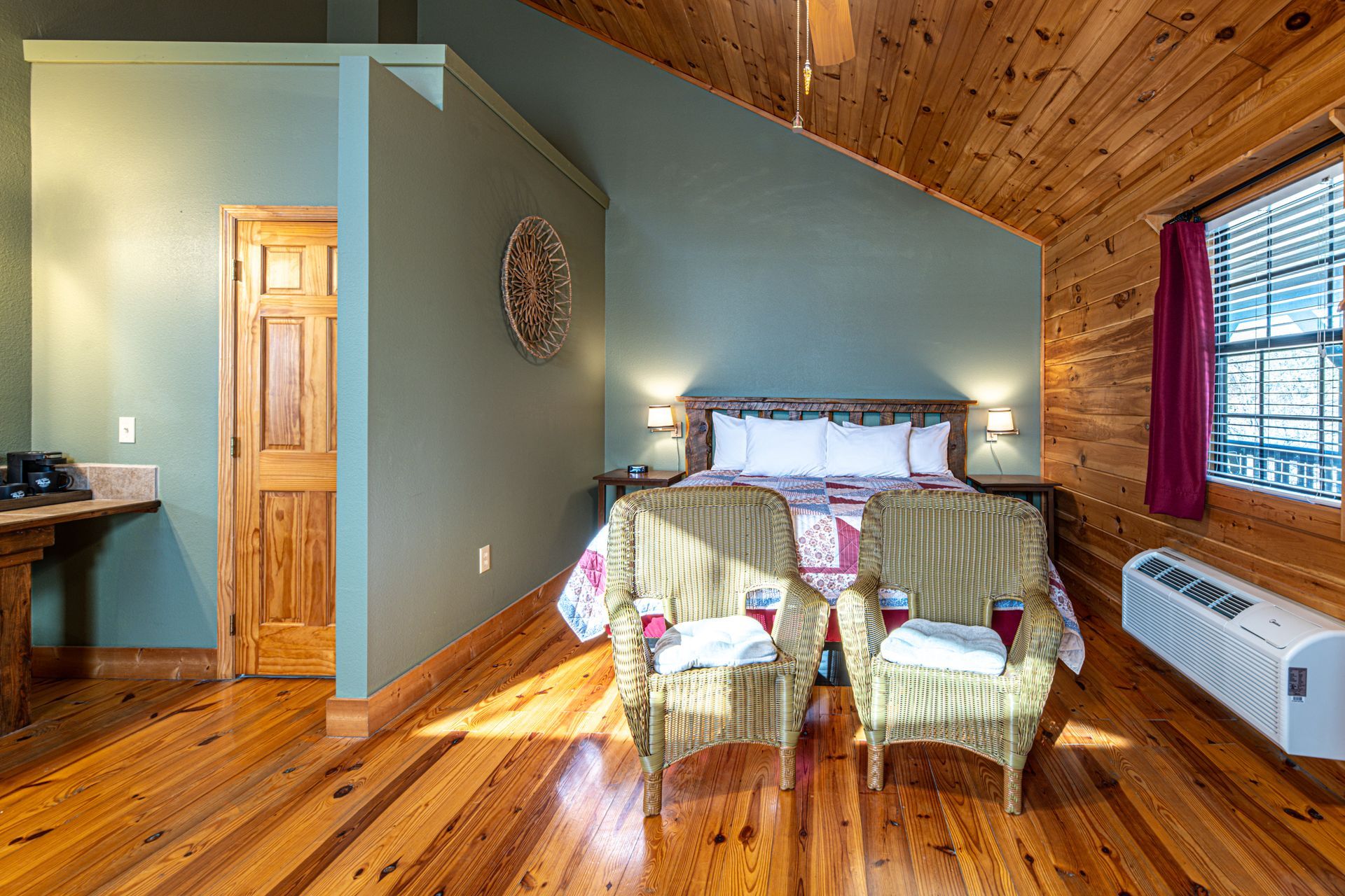 Bedroom with wooden floor, bed, two wicker chairs, and small window.