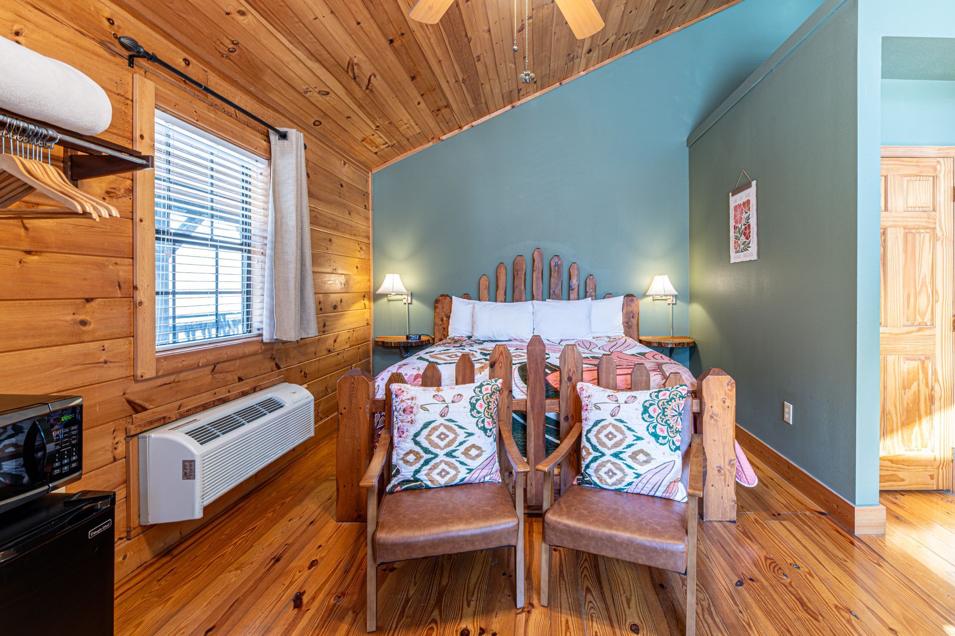 Wooden cabin bedroom with a bed, two chairs, and a window.