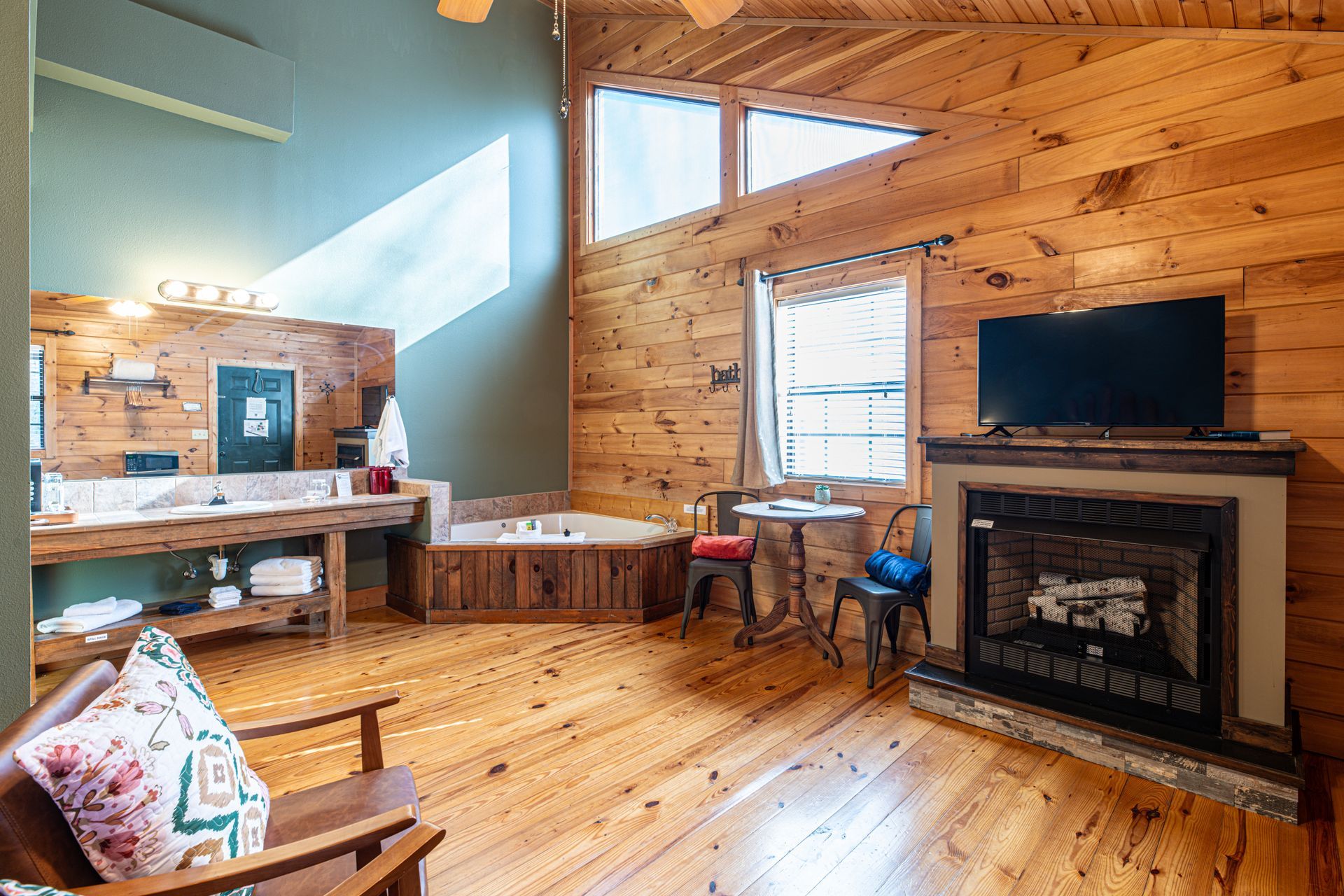 Interior of a cabin-like room with wood paneling, a fireplace, and a large bathtub.