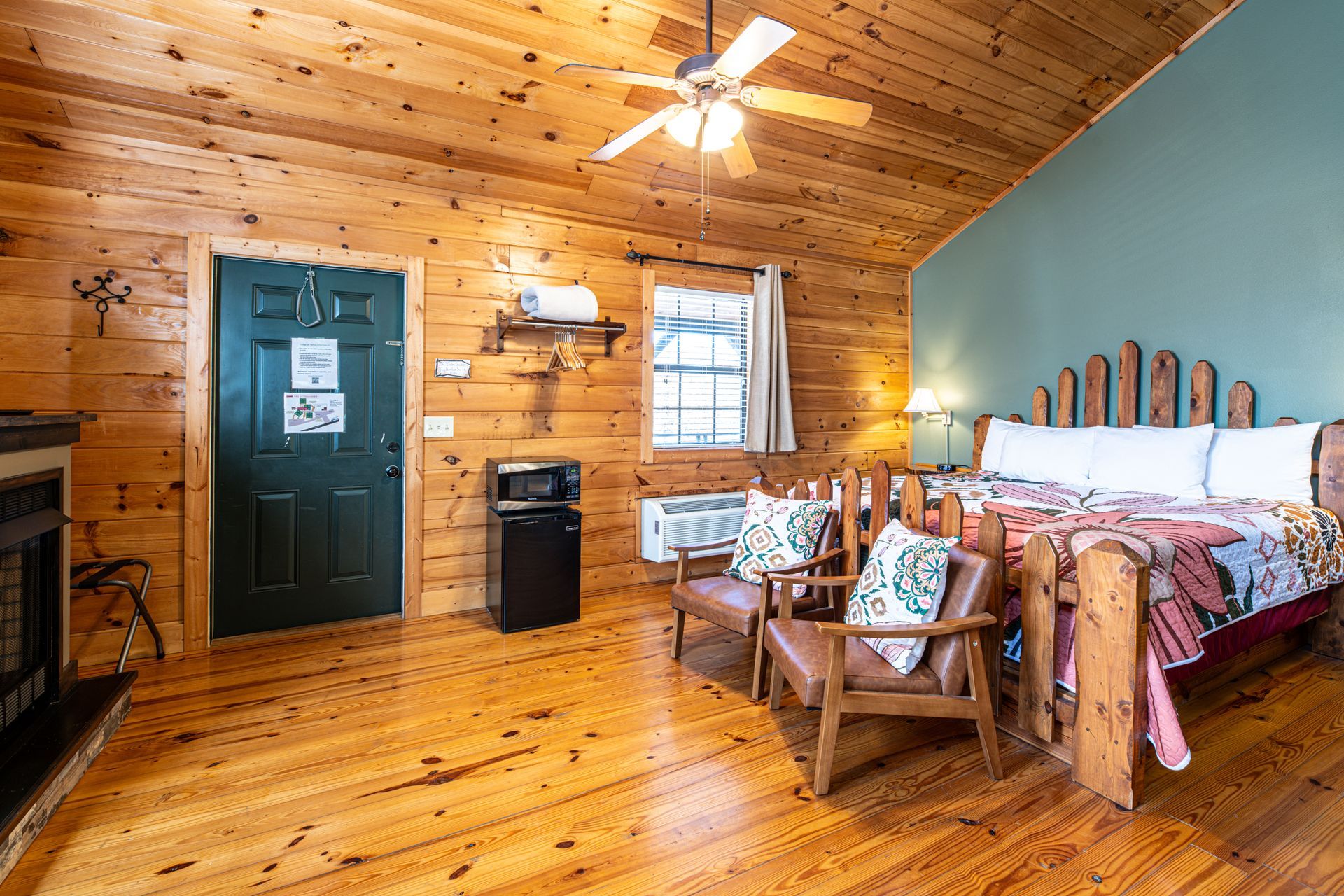 Wooden cabin interior with bed, chairs, fireplace, and microwave.