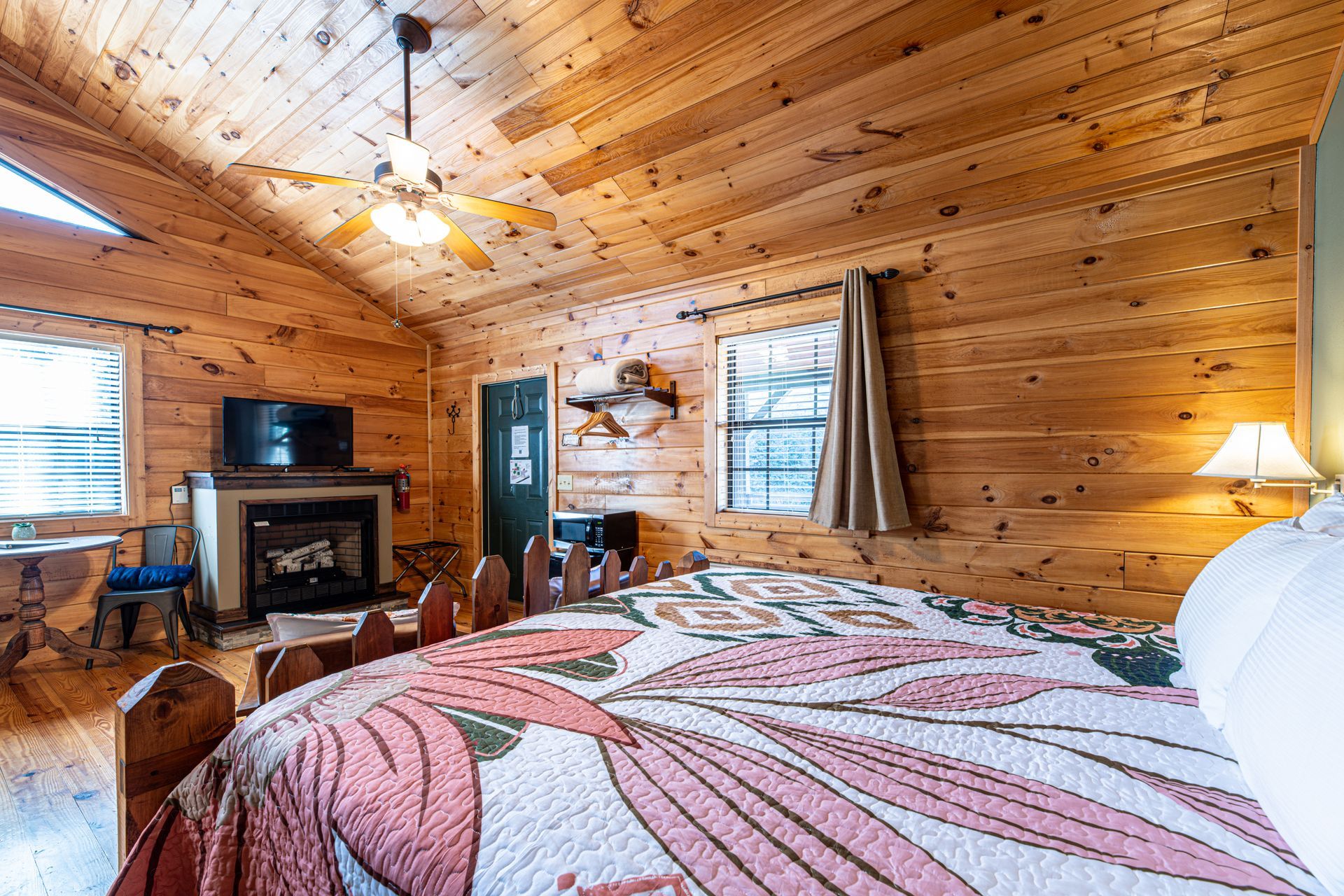 Bedroom with wood paneling, fireplace, and floral quilt.