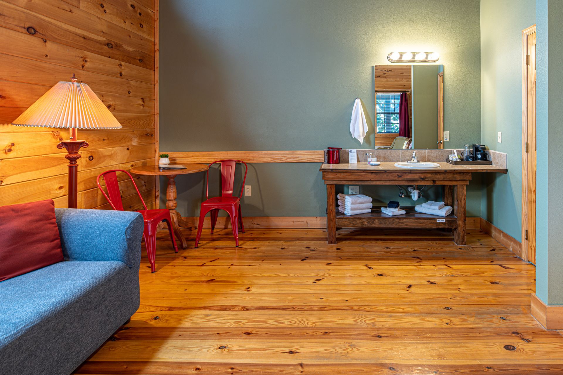 Rustic bathroom with wooden floors and walls, a sofa, a table and red chairs.