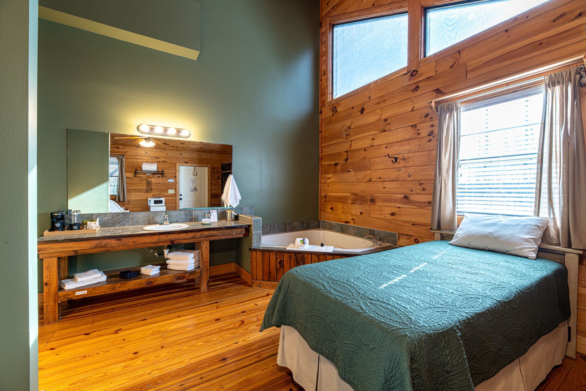 Bedroom with wooden walls, bed, jacuzzi, and a rustic vanity with a large mirror.