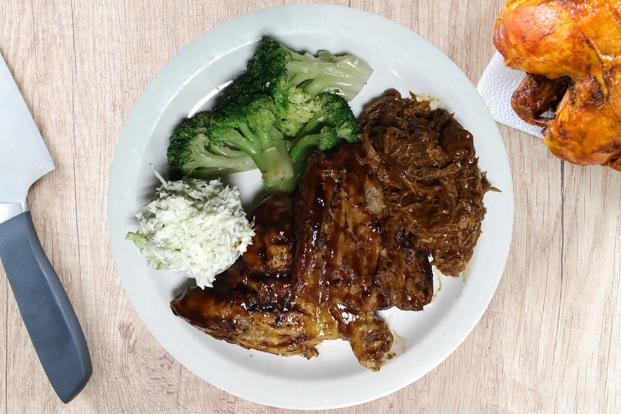 Plate with cooked meat, broccoli, coleslaw, and a chicken. A knife is on the left.