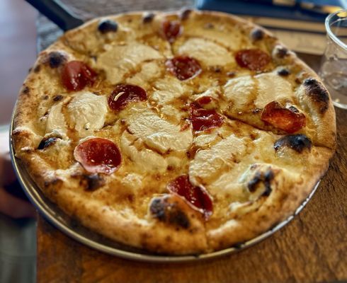 Pizza with pepperoni and creamy cheese on a metal tray on a wooden table.