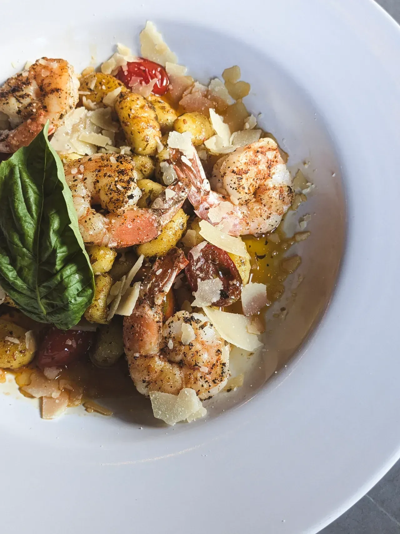 Shrimp and gnocchi pasta dish in white bowl, garnished with basil and parmesan.