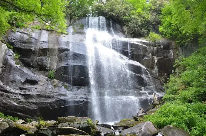 Waterfall cascading down dark, rocky cliffs; lush green foliage surrounds the falls.