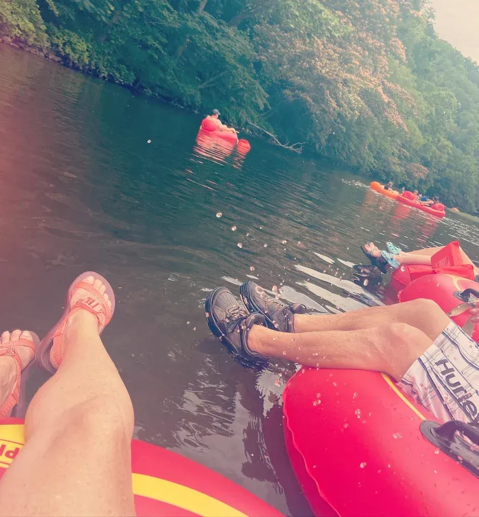 People floating on red inner tubes in a river, surrounded by trees.