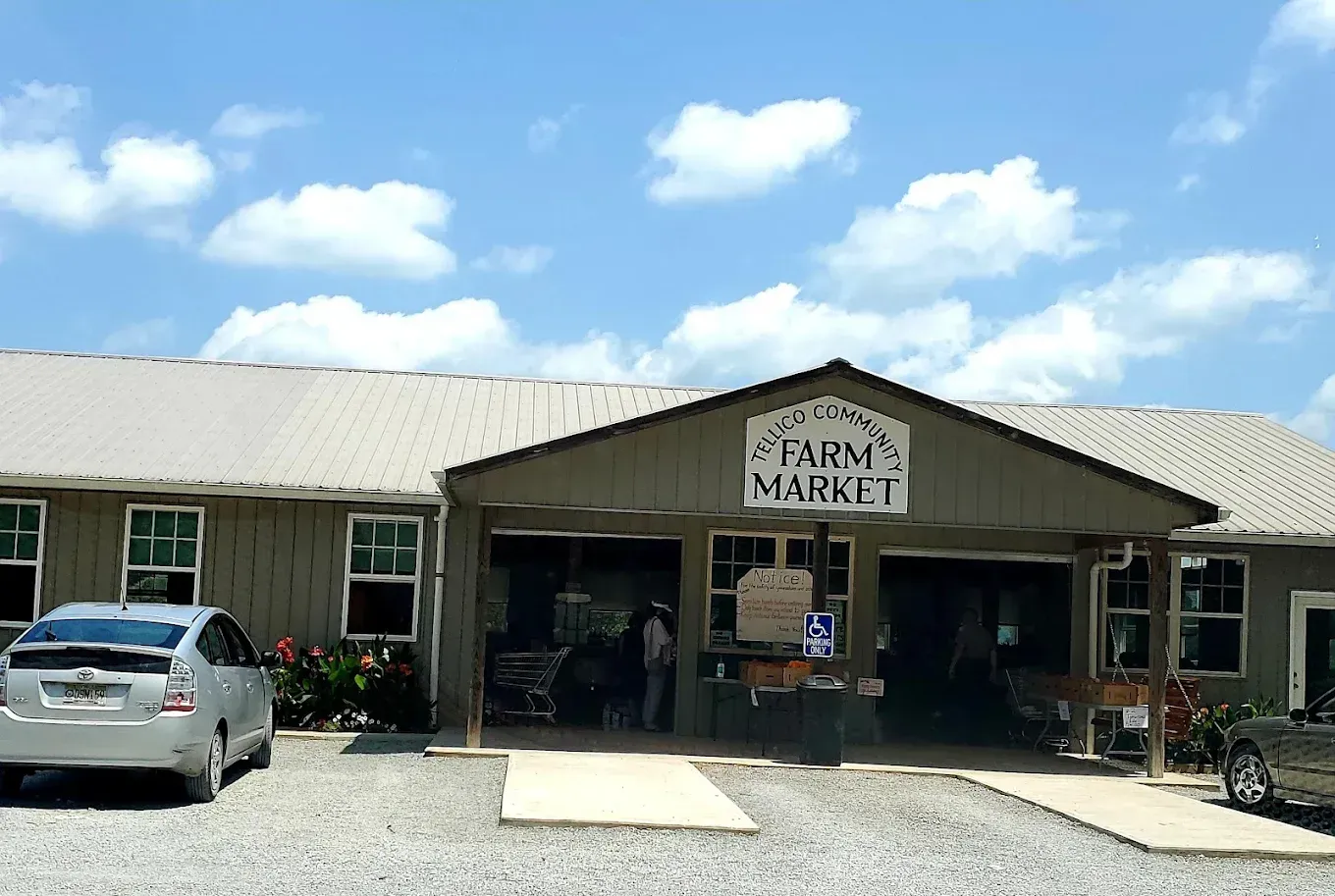 Farm market building with sign and parked car under a blue sky.
