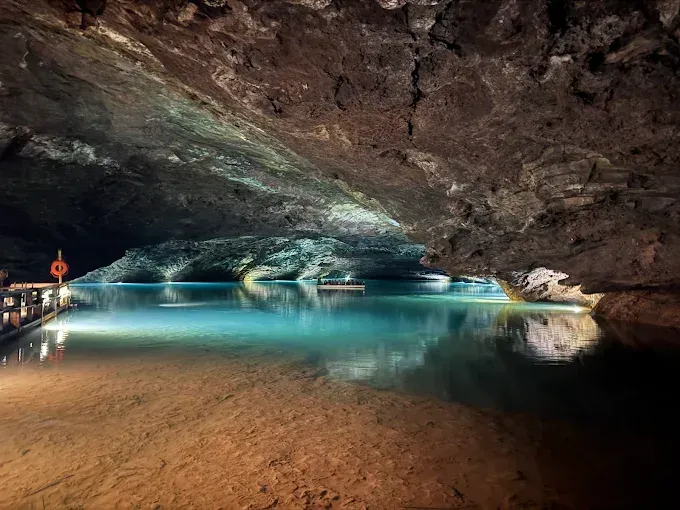 A turquoise lake within a cavern, lit by underwater lights. Wooden walkway and boat visible.