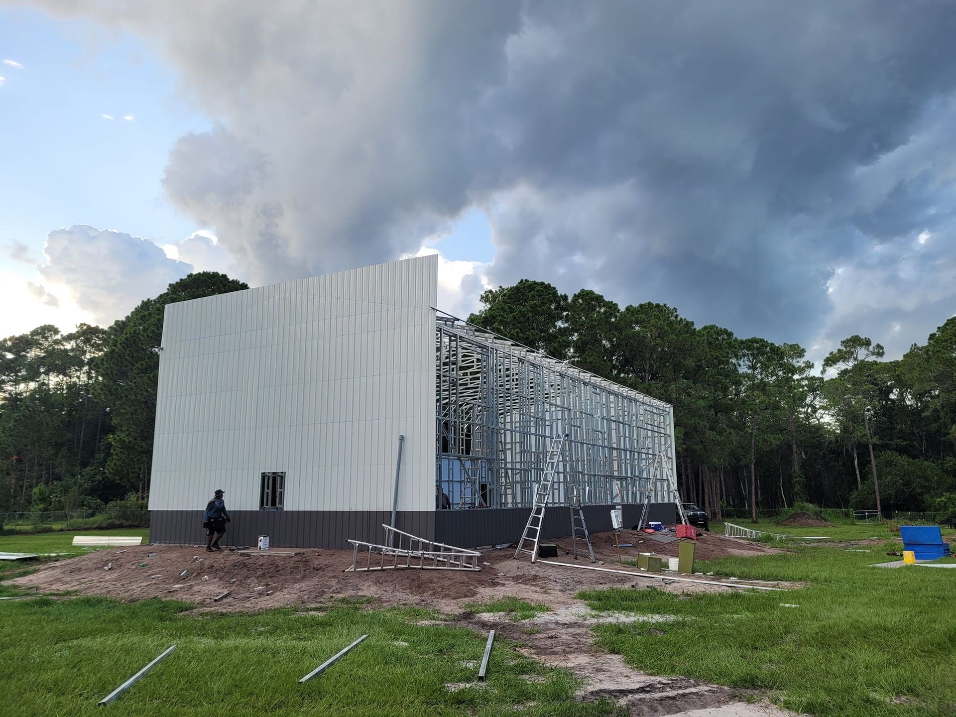 A large white building is being built in a field with trees in the background.
