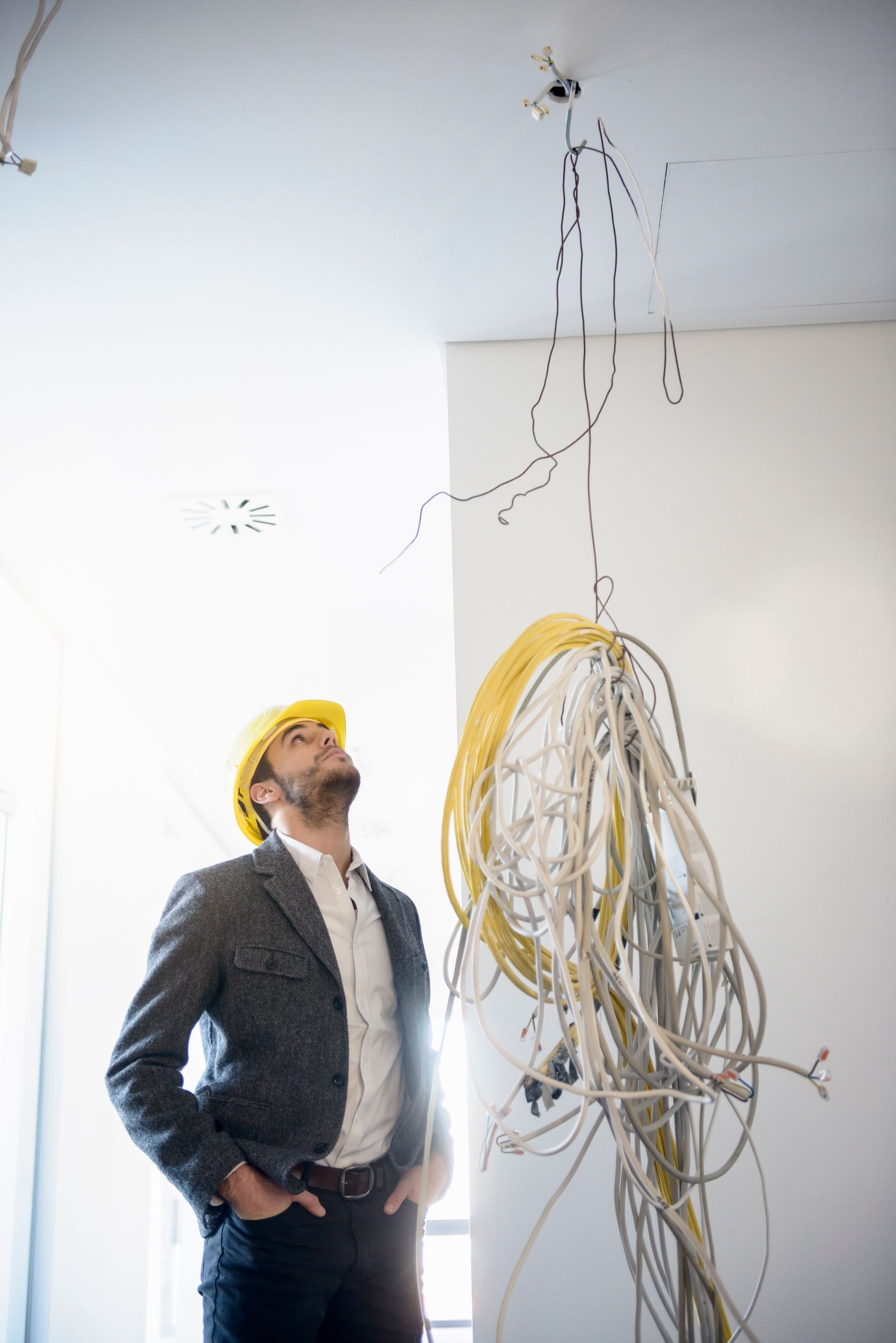 A man in a hard hat is looking up at a bunch of wires hanging from the ceiling.