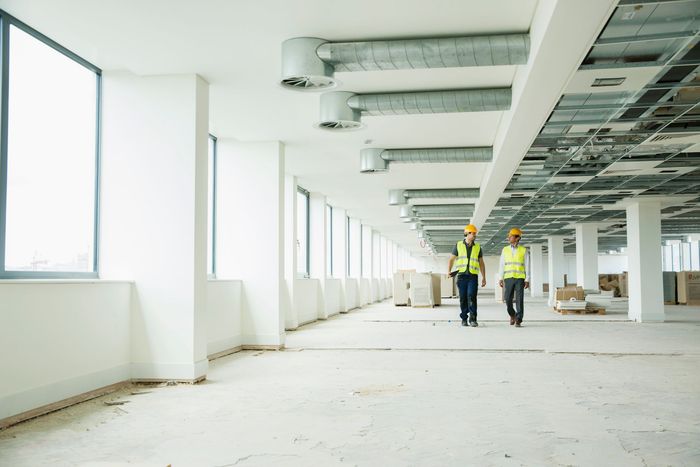 Two construction workers are walking through an empty building.