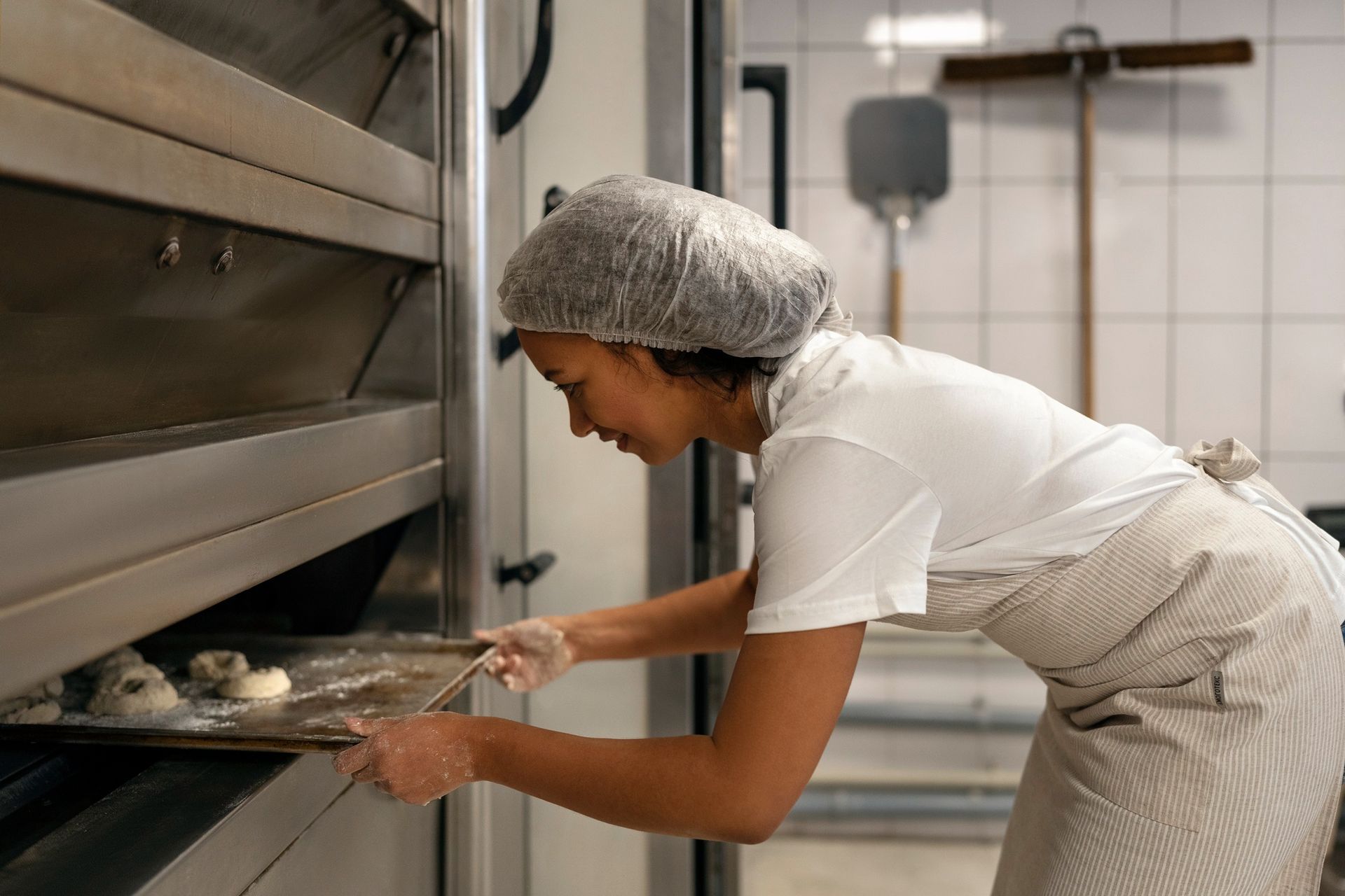 a woman is putting dough into an oven in a bakery .