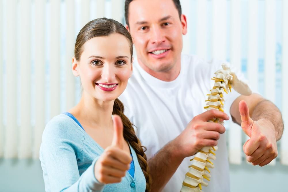 A Man And A Woman Are Giving A Thumbs Up While Holding A Model Of A Spine — Trinity Family Chiropractic In Brinsmead, QLD