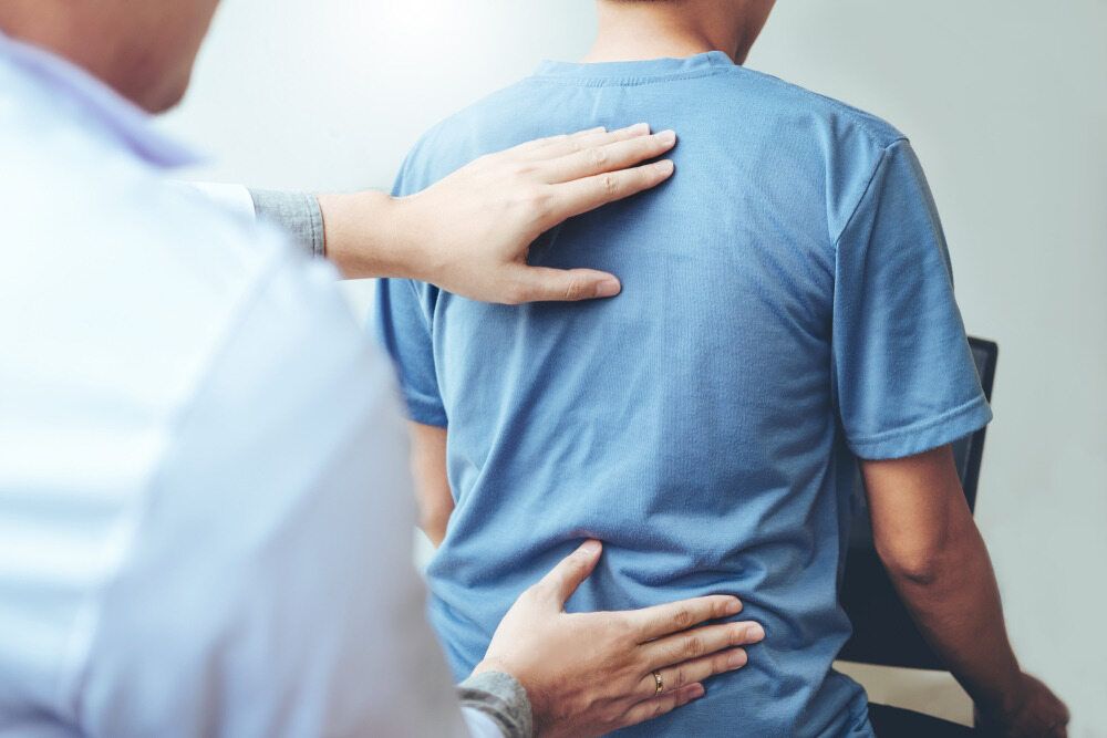 A Man In A Blue Shirt Is Getting His Back Examined By A Doctor — Trinity Family Chiropractic In Cairns, QLD