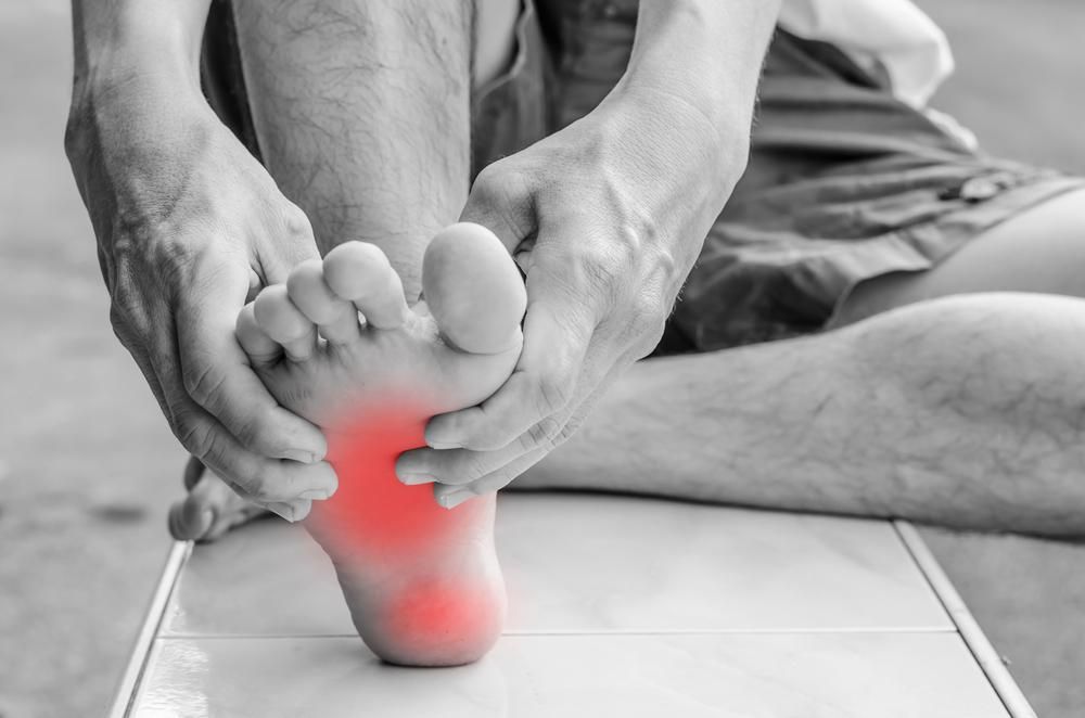 A Man Is Sitting On The Floor Holding His Foot In Pain — Trinity Family Chiropractic In Cairns, QLD