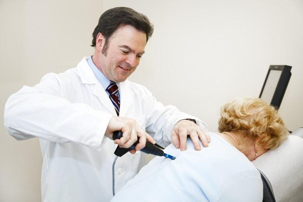 A Doctor Is Examining A Patient's Back With A Device — Trinity Family Chiropractic In Redlynch, QLD