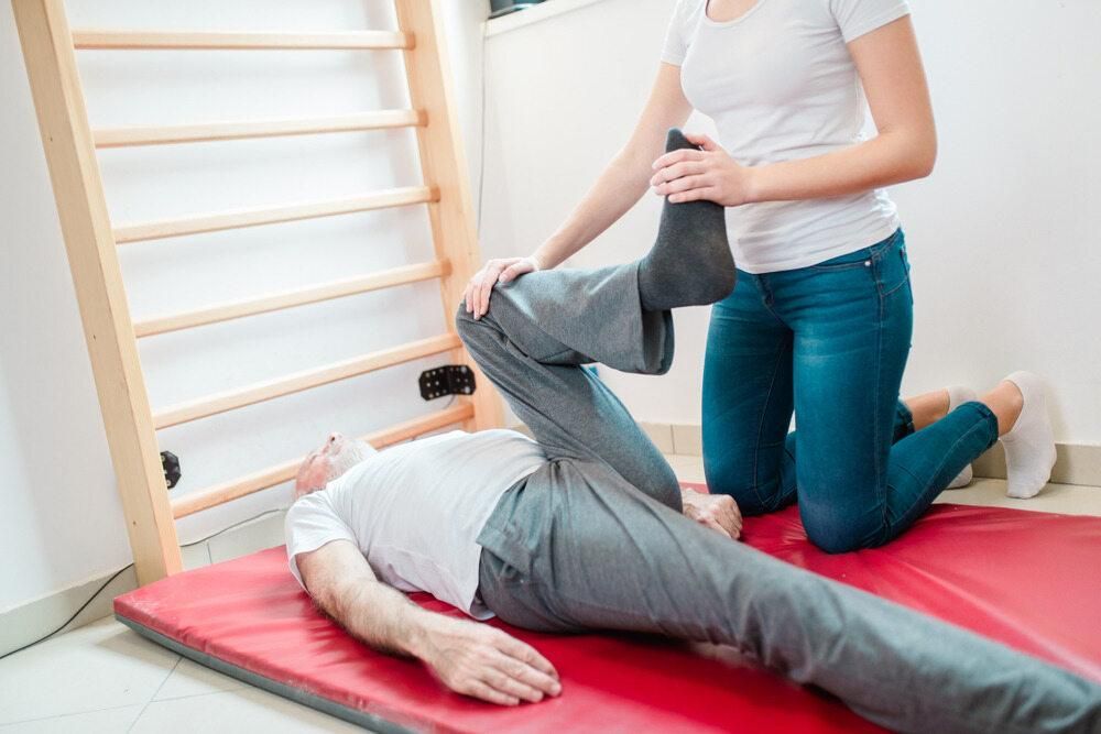 A Person Performing Chiropractic Services On A Man Laying On the Ground With One Leg Up — Trinity Family Chiropractic In Cairns, QLD