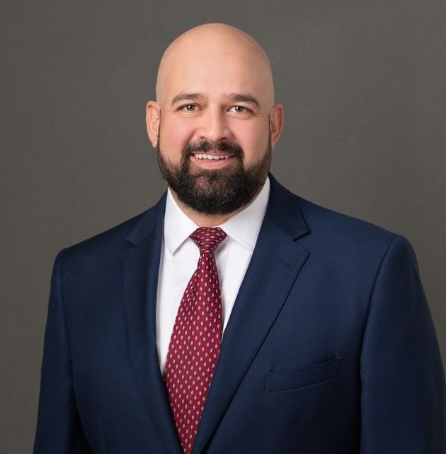 A bald man with a beard wearing a blue suit and red tie