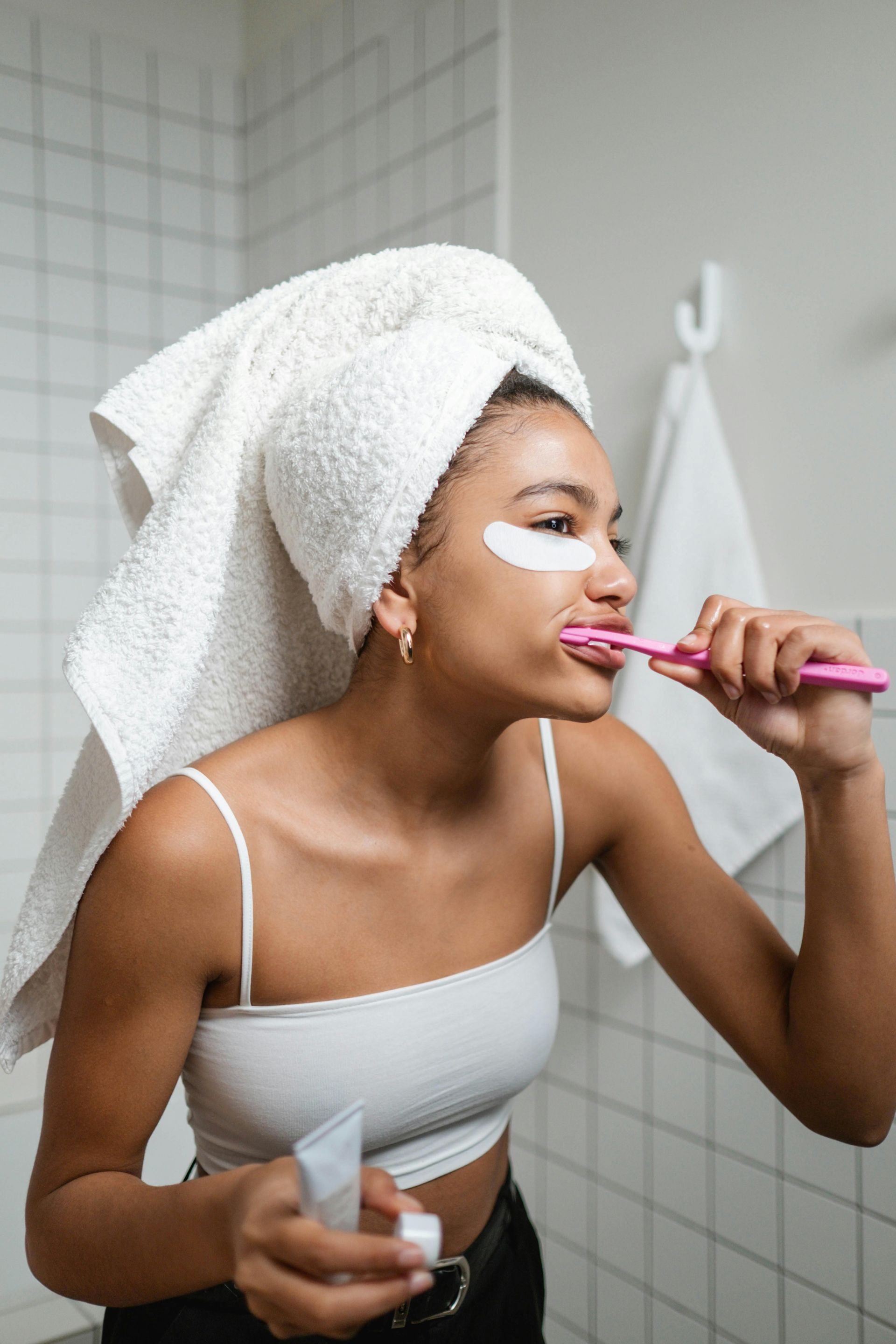 A woman with a towel wrapped around her head is brushing her teeth in the bathroom.