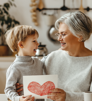 An elderly woman is holding a card with a heart drawn on it.