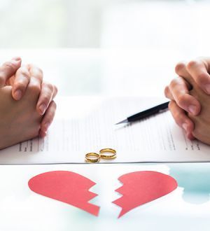 Two people are sitting at a table with a broken heart and wedding rings.