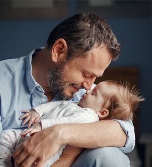 A man is holding a baby in his lap and the baby is kissing the man on the cheek.