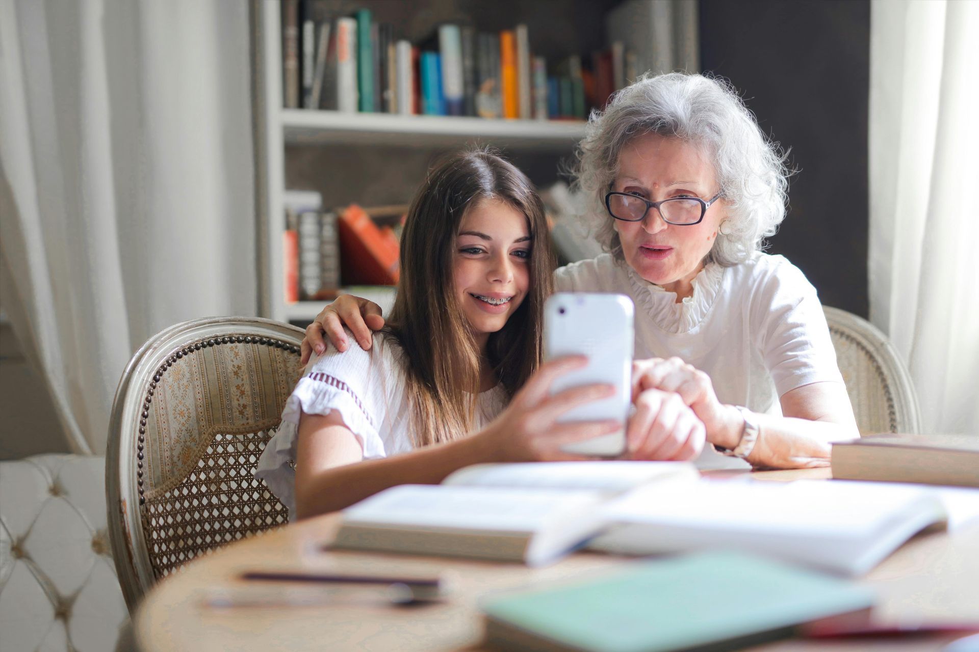 An elderly woman and a young girl are sitting at a table looking at a cell phone.