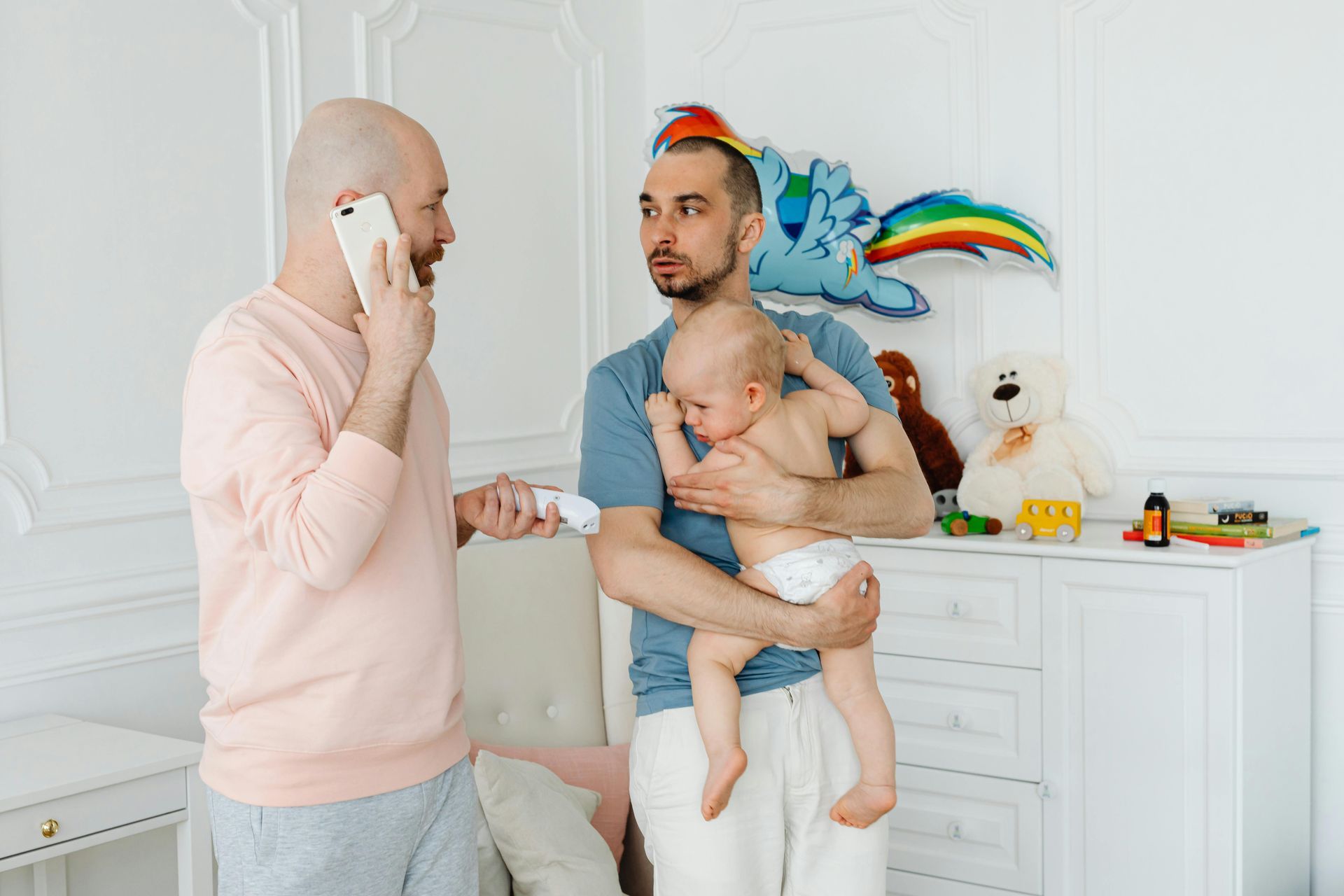 Two men are holding a baby and one is talking on a cell phone.