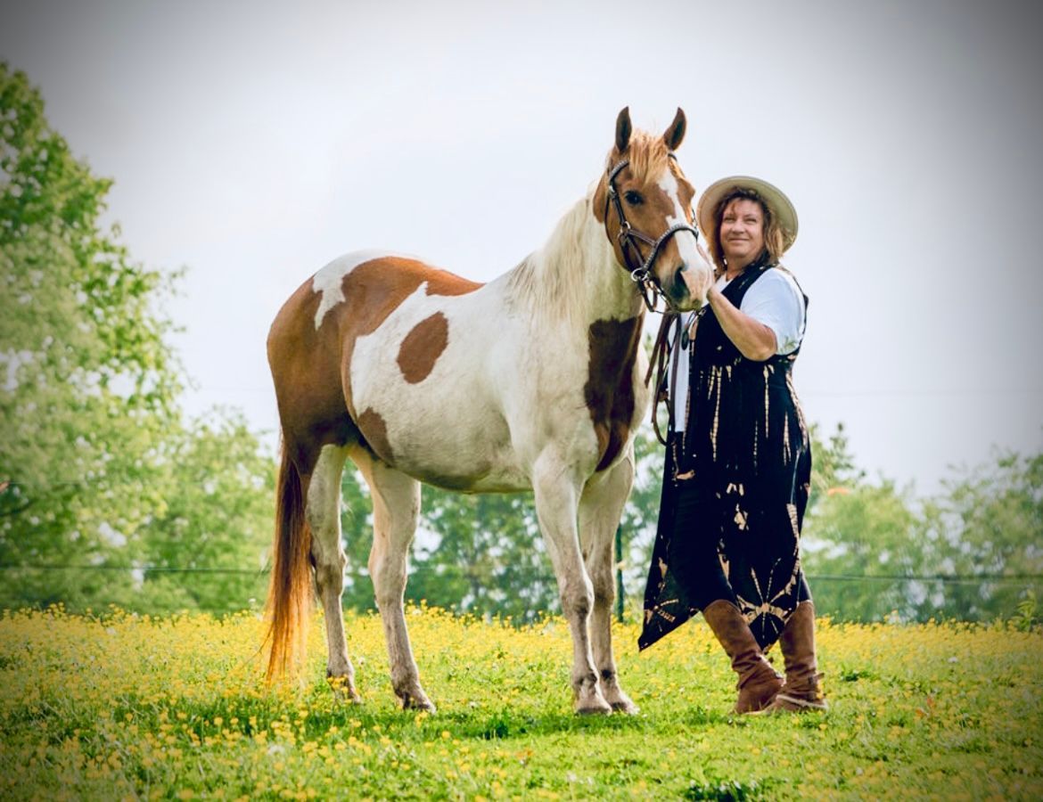 A woman is standing next to a brown and white horse in a field.