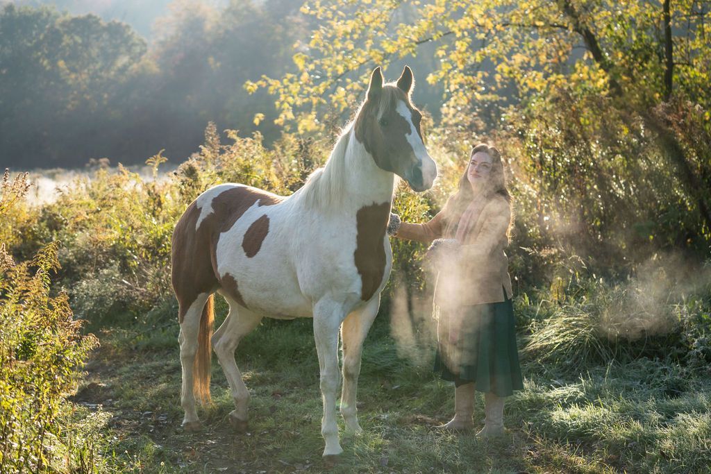 A woman is standing next to a brown and white horse in a field.