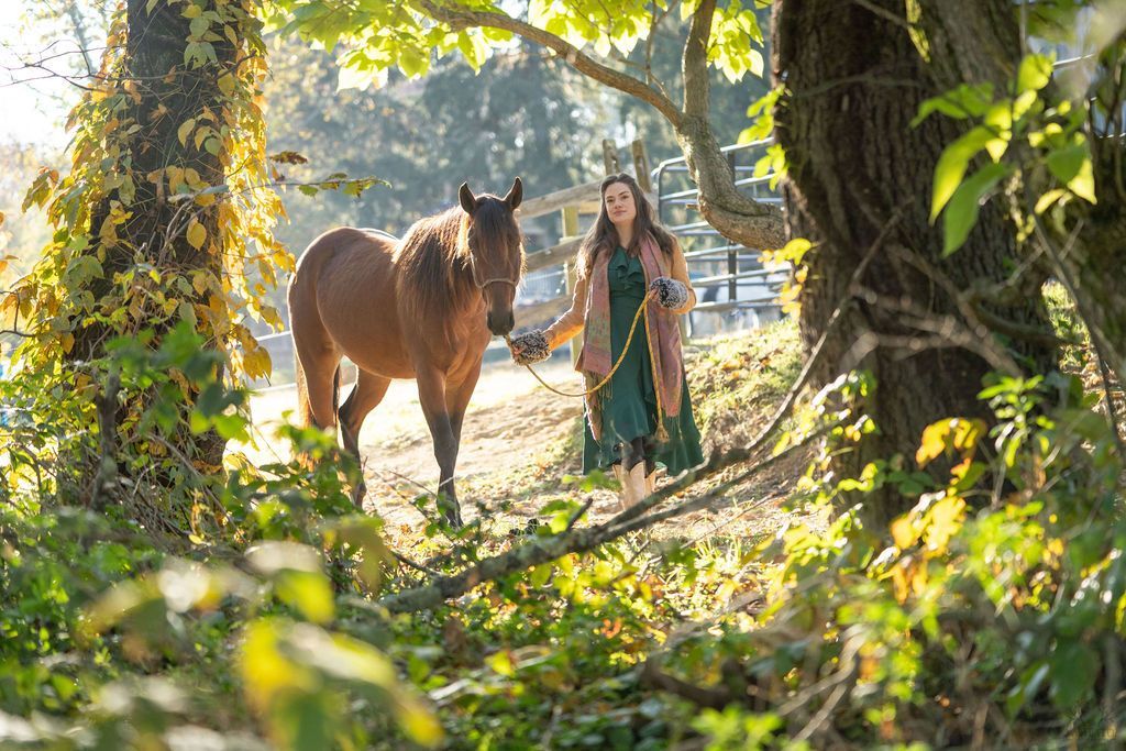 A woman is standing next to a horse in the woods.