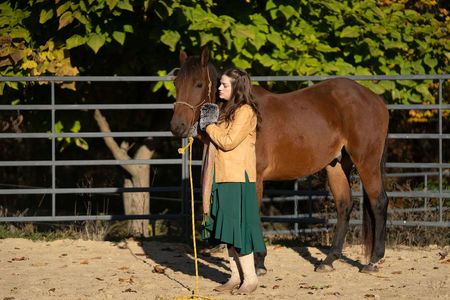 A woman in a green skirt is standing next to a brown horse.