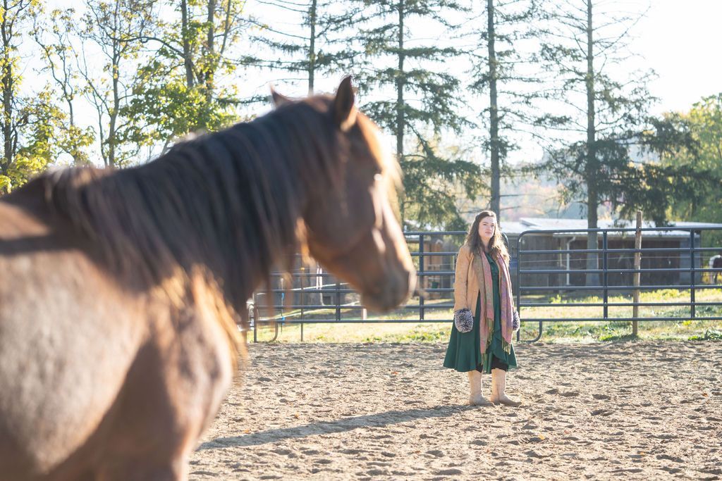 A woman is standing next to a brown horse in a dirt field.
