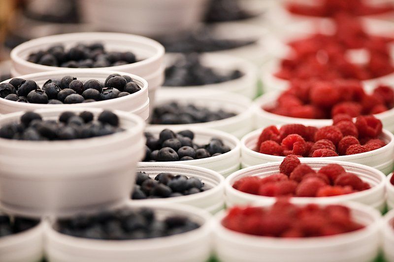 Blueberries and raspberries in white containers, at a market or store, close up.