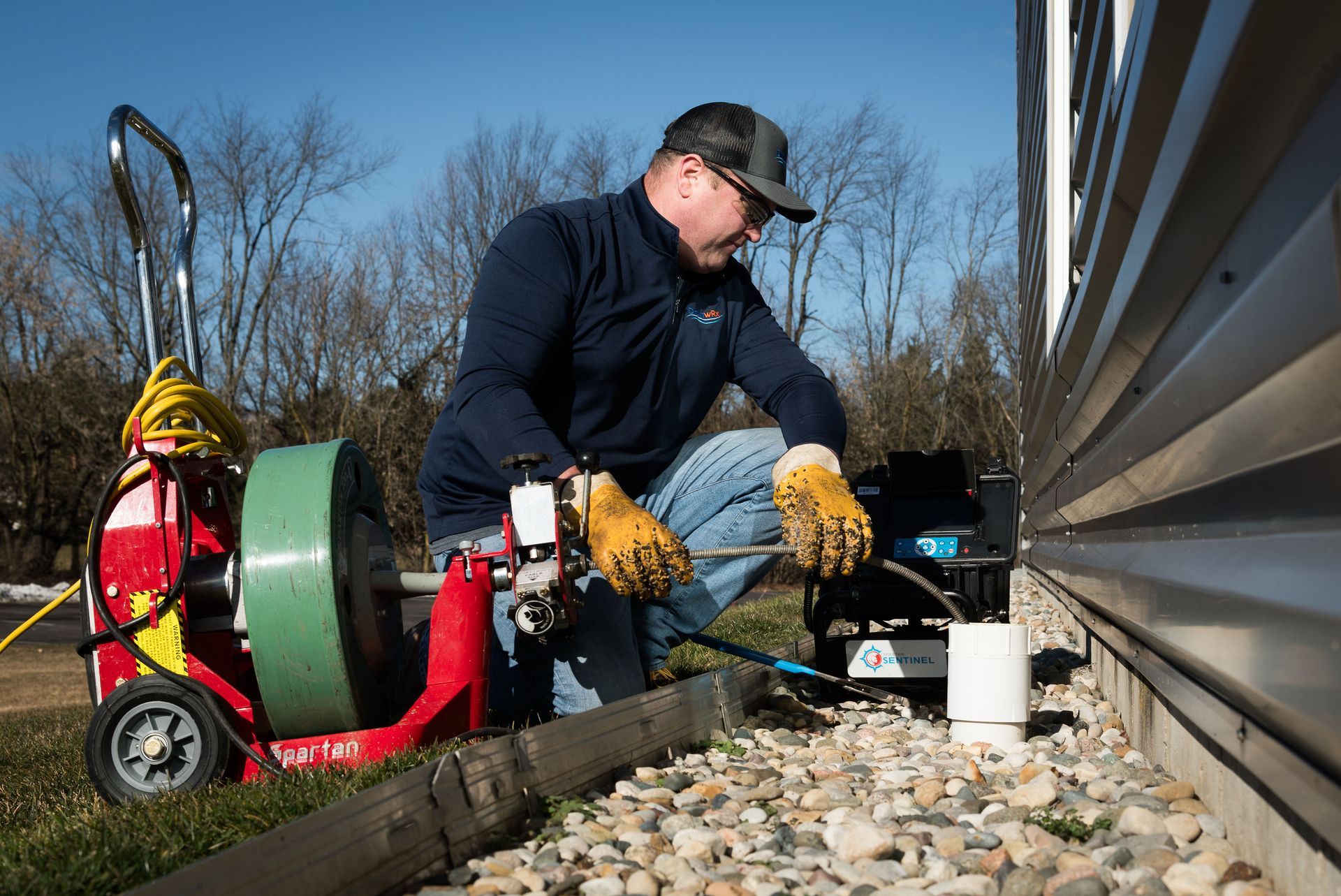 A man is using a drain cleaner to clean a drain outside of a building.