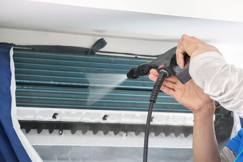 A person is cleaning an air conditioner with a high pressure washer.