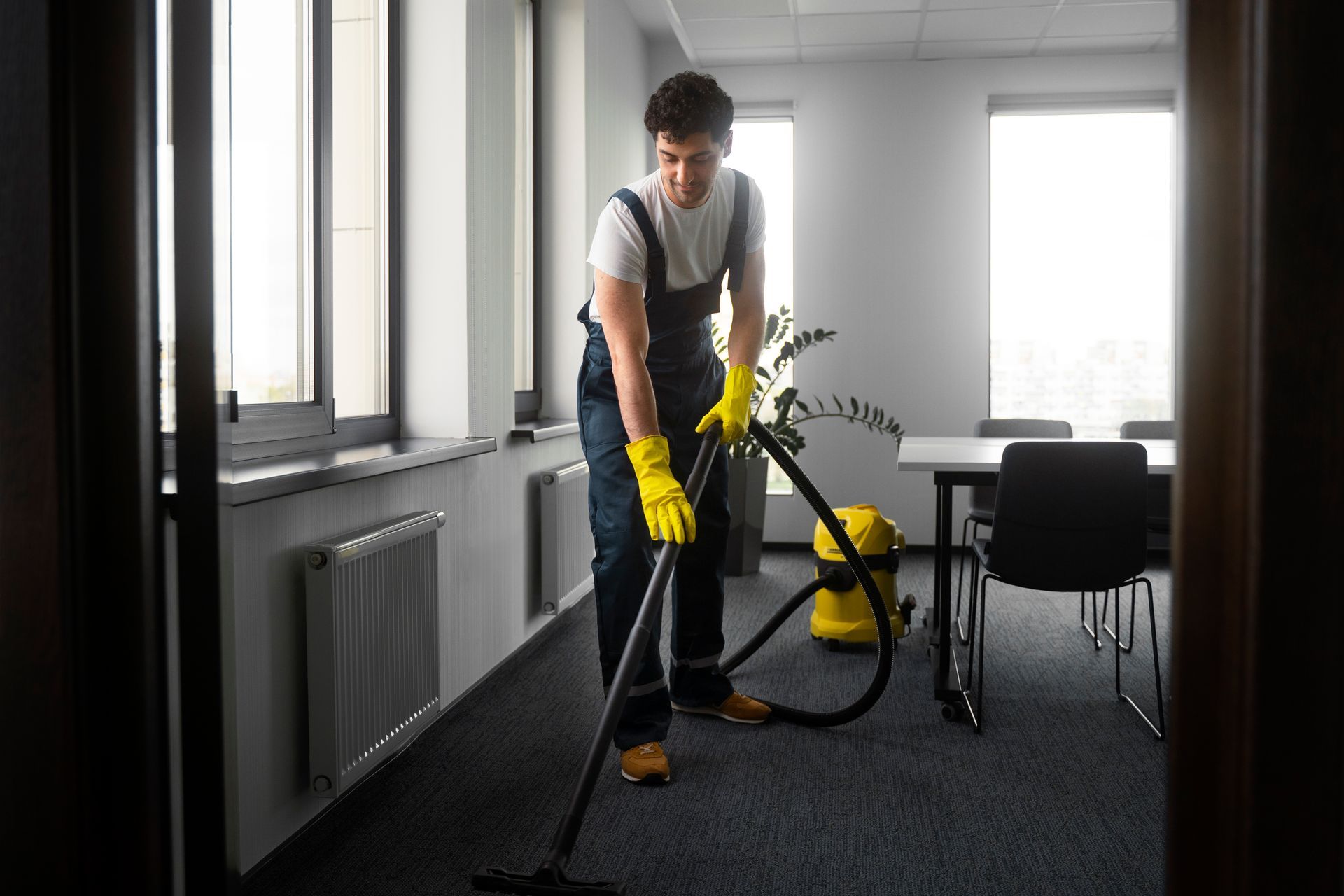 Man in yellow gloves vacuums office carpet.