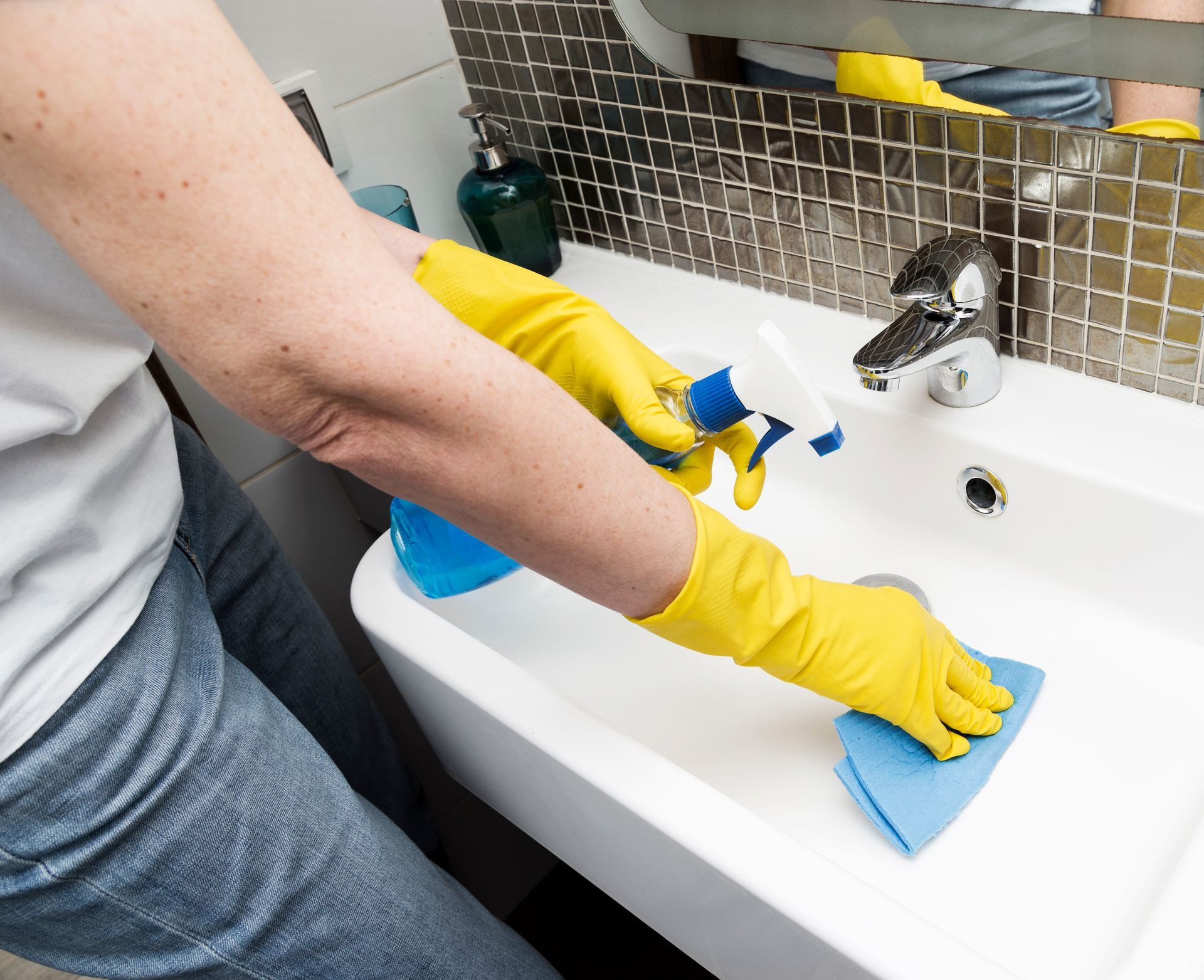A woman wearing yellow gloves is cleaning a bathroom sink
