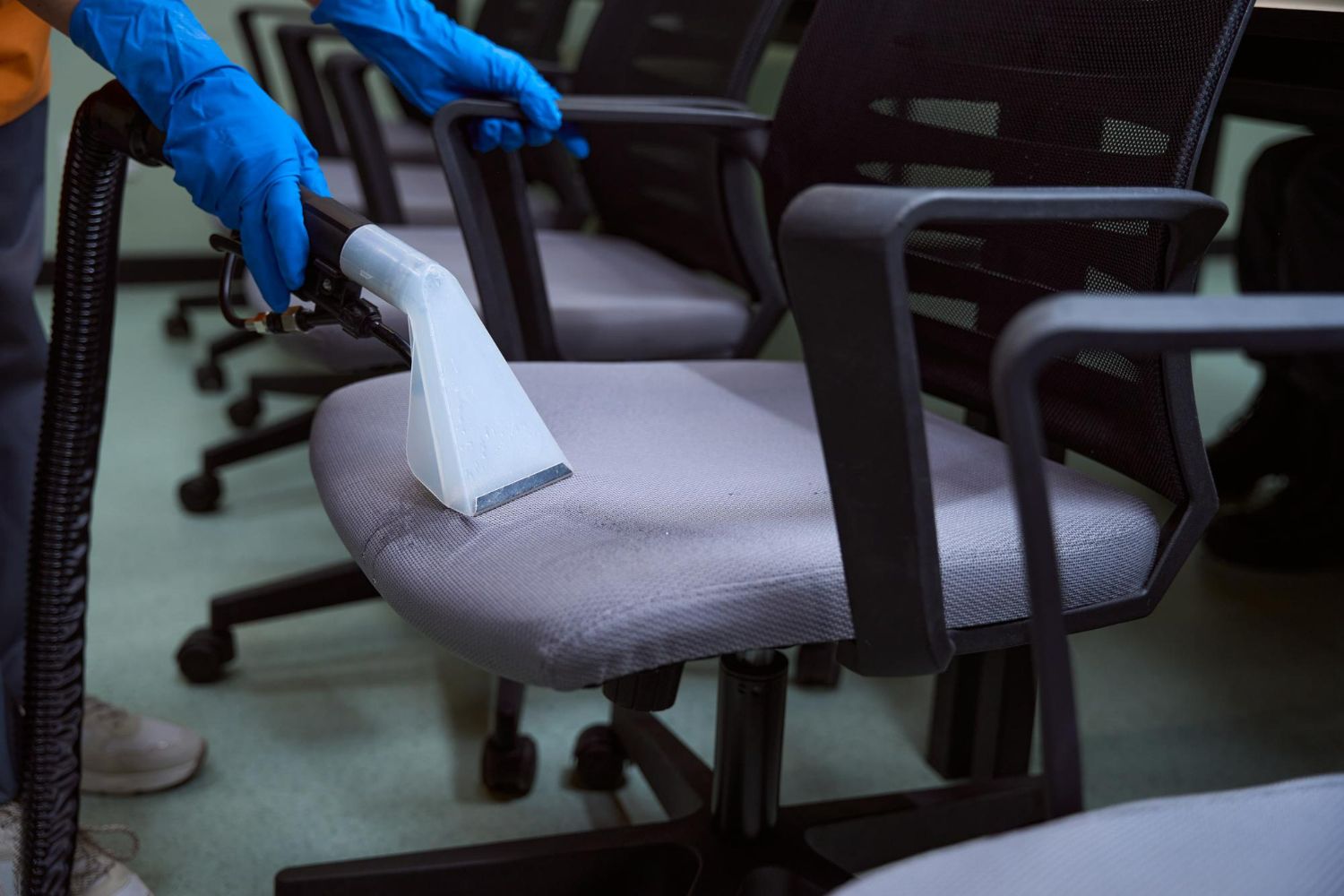 A person is cleaning an office chair with a vacuum cleaner.