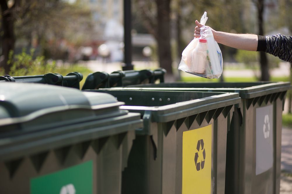 A person is throwing a plastic bag into a recycling bin.