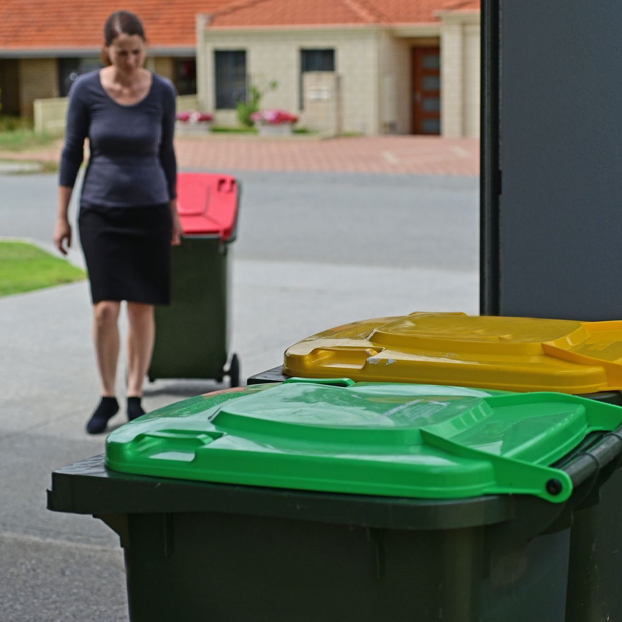 a woman rolls a garbage can into a garage