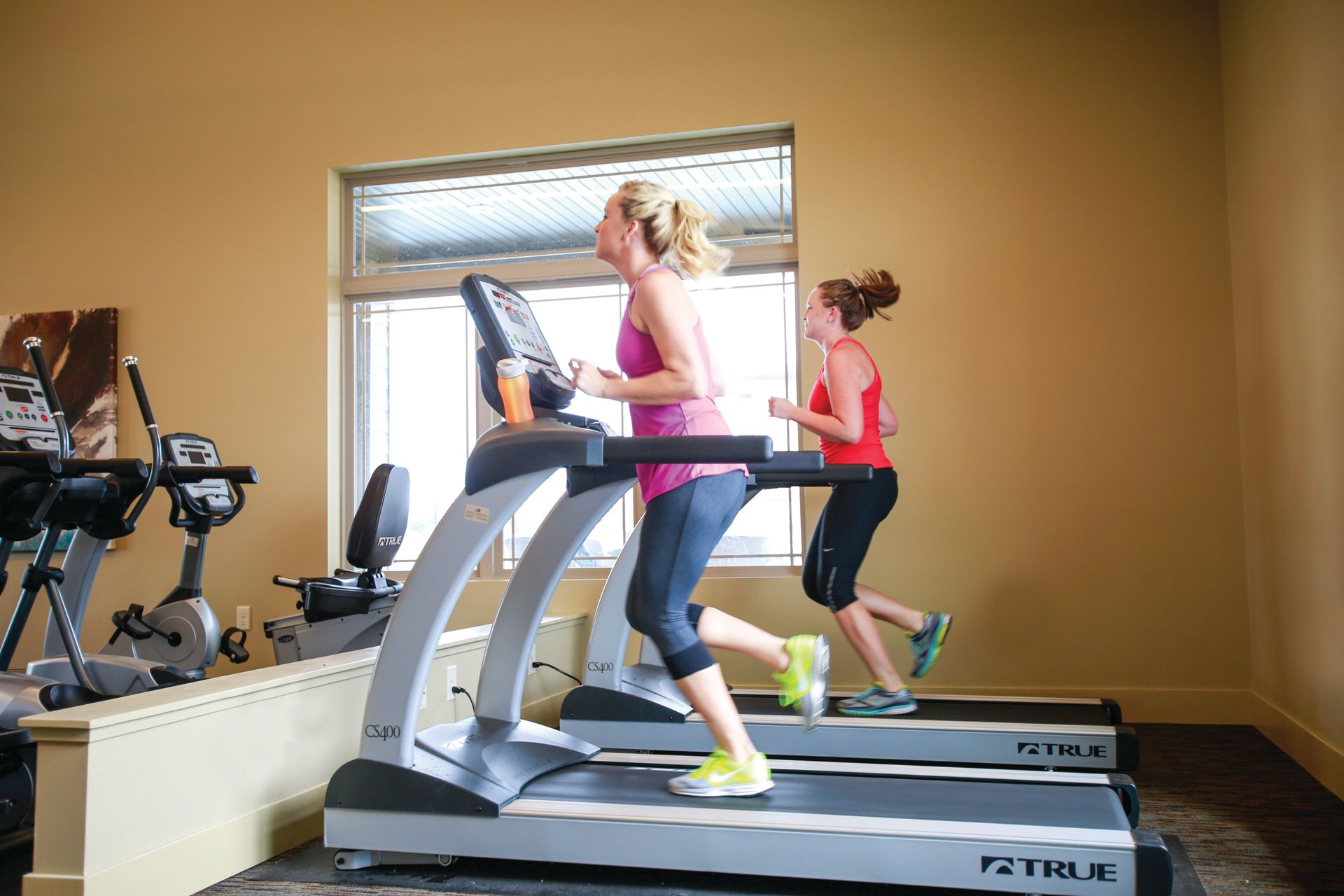Two women are running on treadmills in a gym.