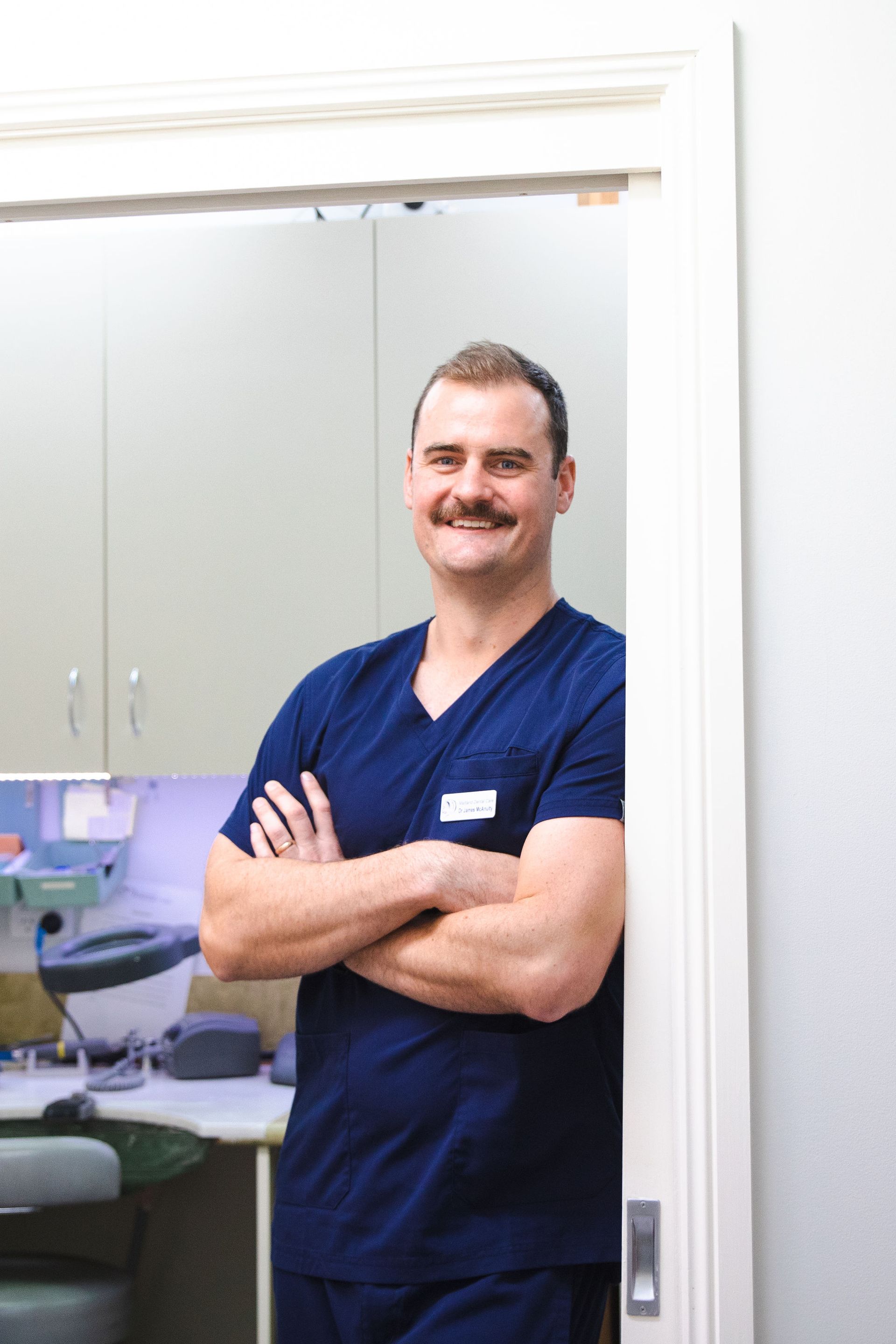 A man in scrubs is standing in a doorway with his arms crossed — Maitland Dental Care In Maitland NSW